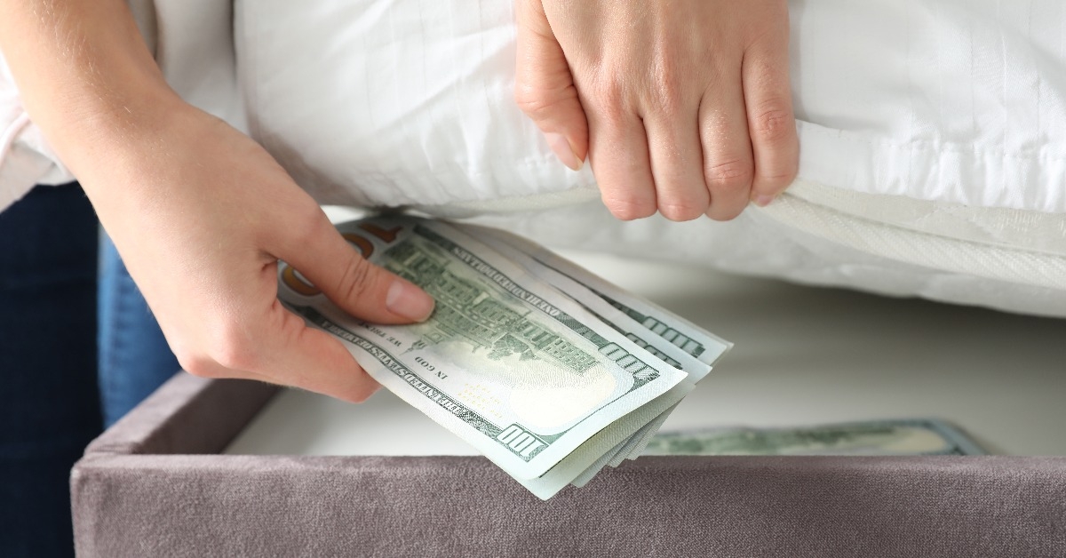 Woman hiding dollar banknotes under mattress in bedroom