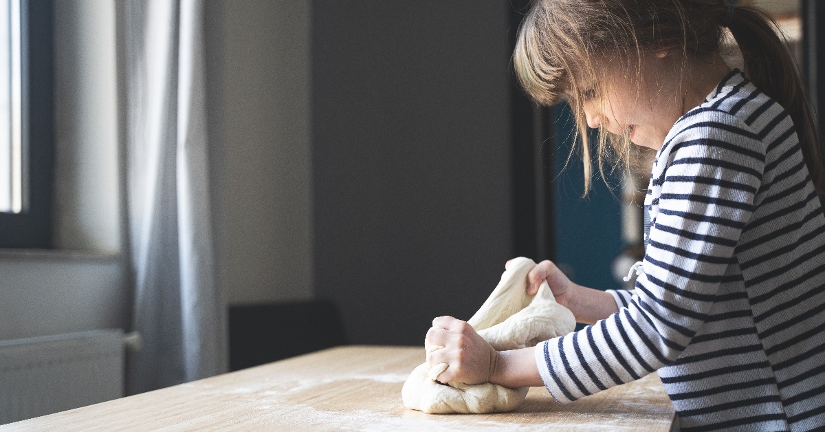 little girl working the dough on a wood cutting board