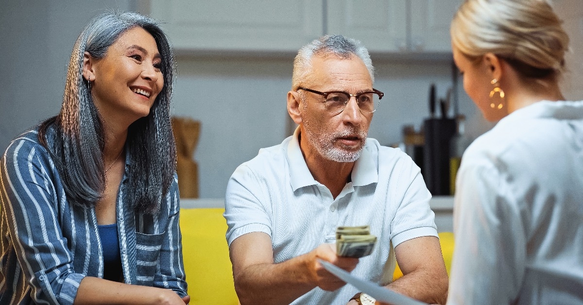 asian woman smiling near elderly husband giving money to insurance agent
