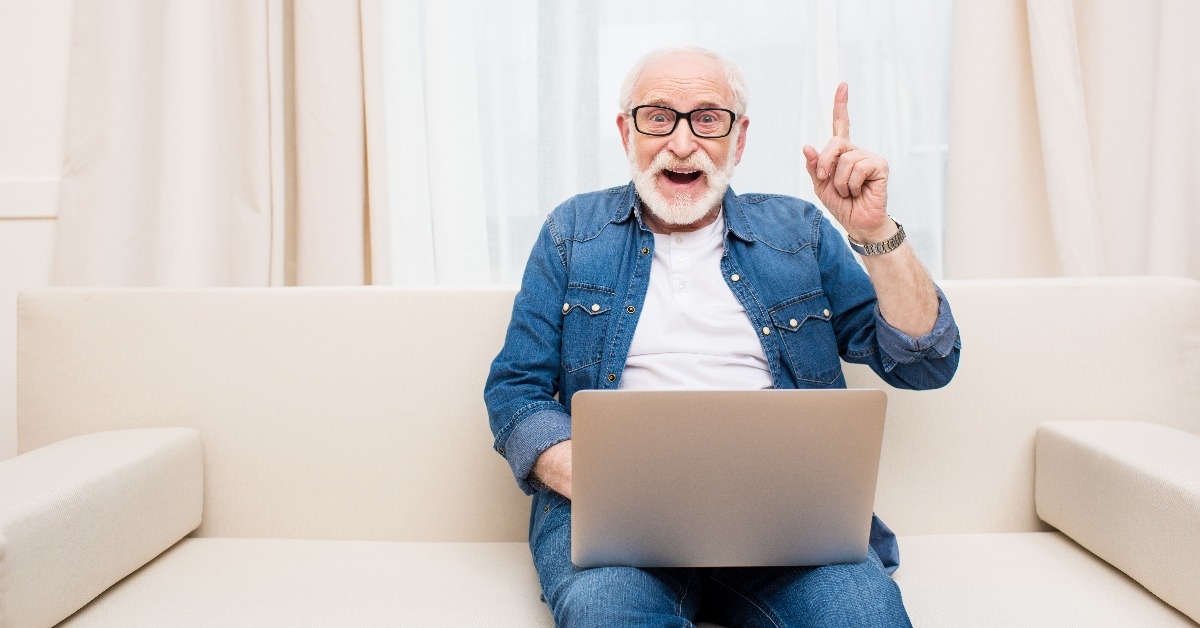 Smiling senior man using laptop and pointing up with finger