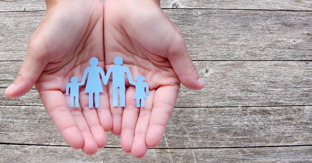 Paper family in hands on wooden background welfare concept