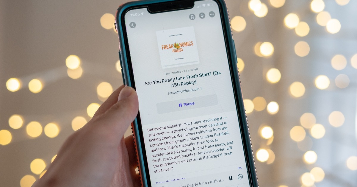 Hand holds a smartphone using the Apple Podcast app to listen to Freakonomics