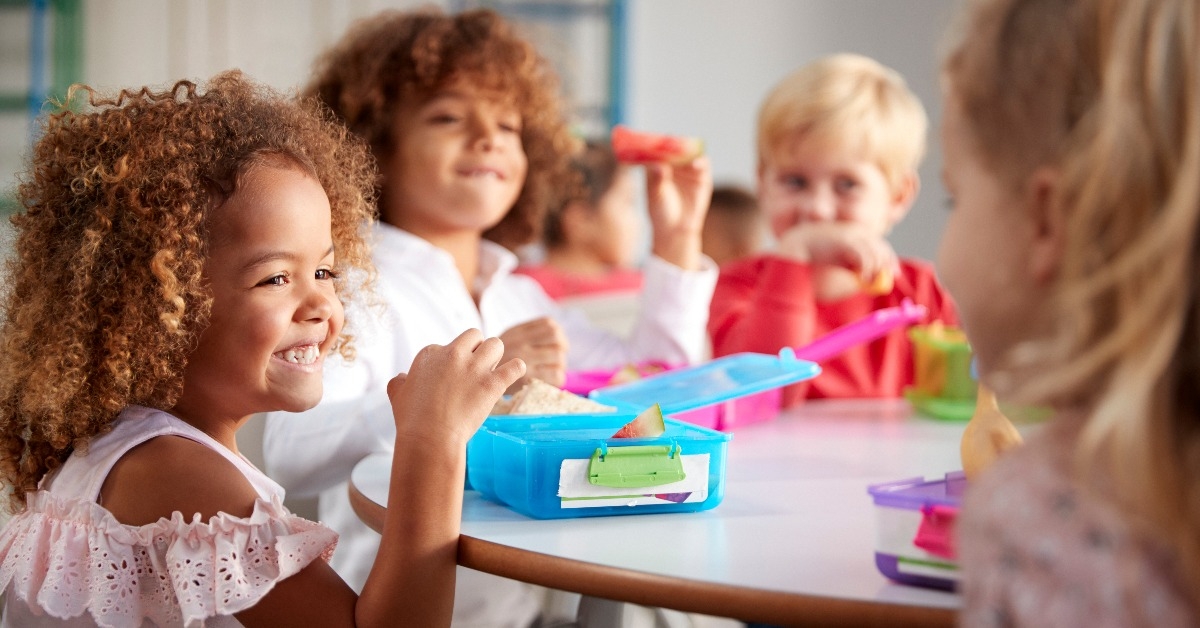 young children sitting at a table eating their packed lunches together