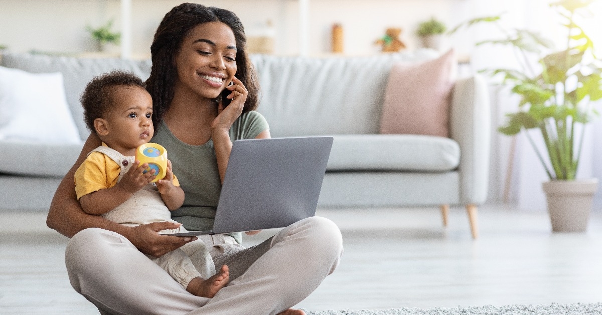 happy black woman with baby working with laptop and cellphone