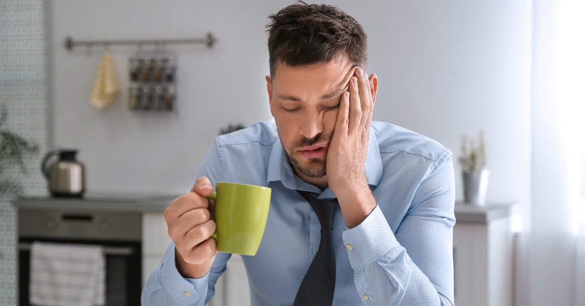 sleepy man with cup of drink at home in morning