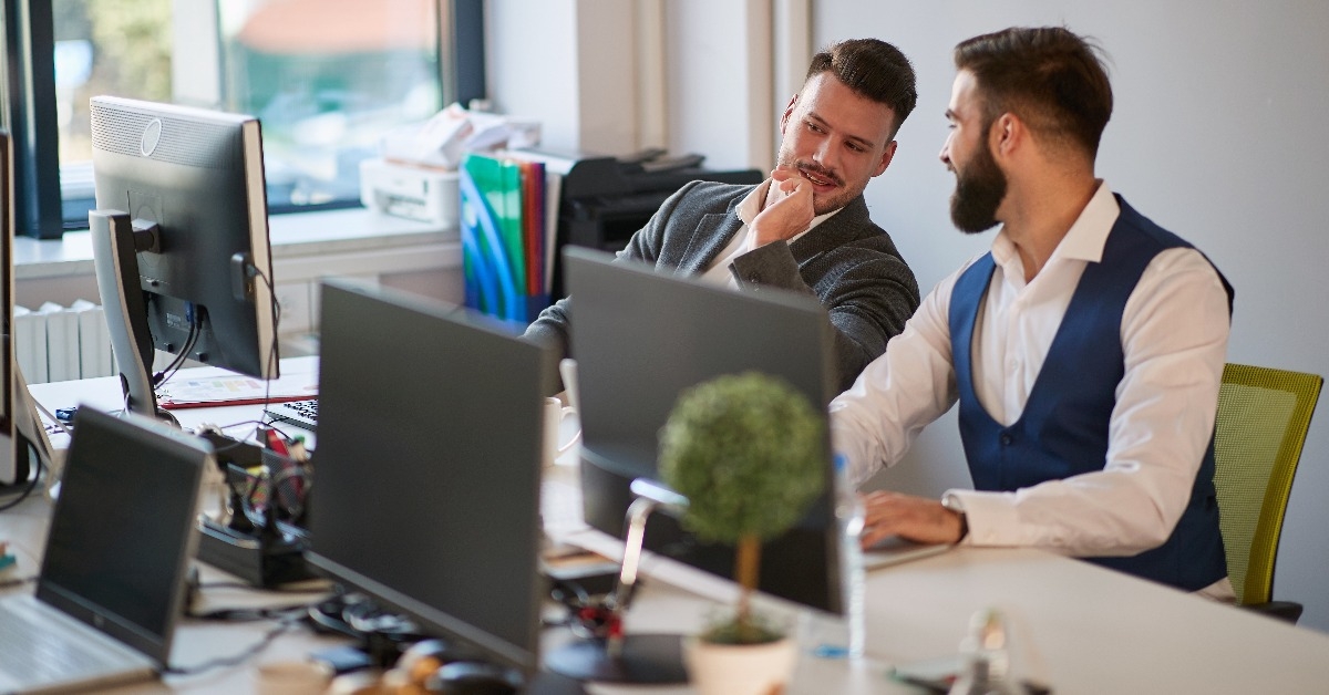two male colleagues gossip at work in open space office