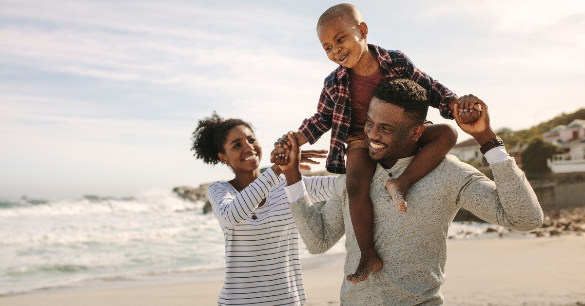 parents carrying son on shoulders on beach vacation