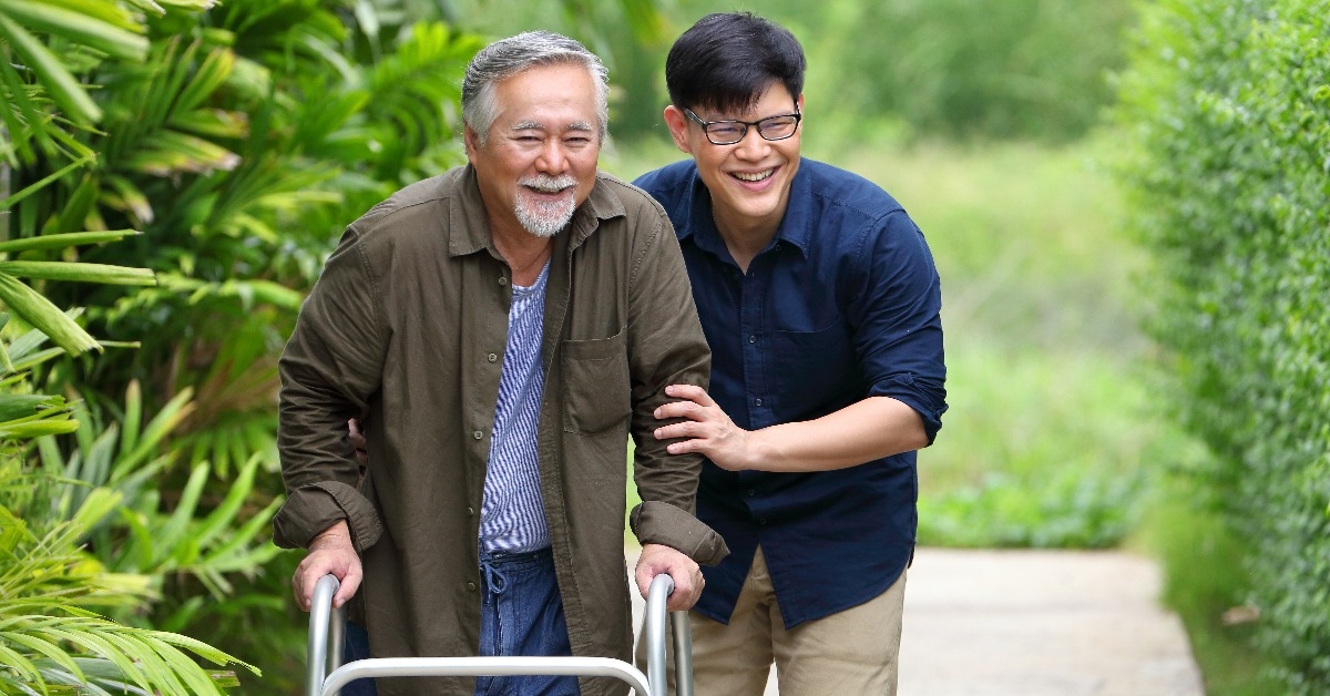 senior man using walker while walking for exercise around the garden with his son