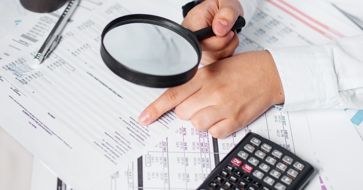 businessman using magnifying glass to review balance sheet 