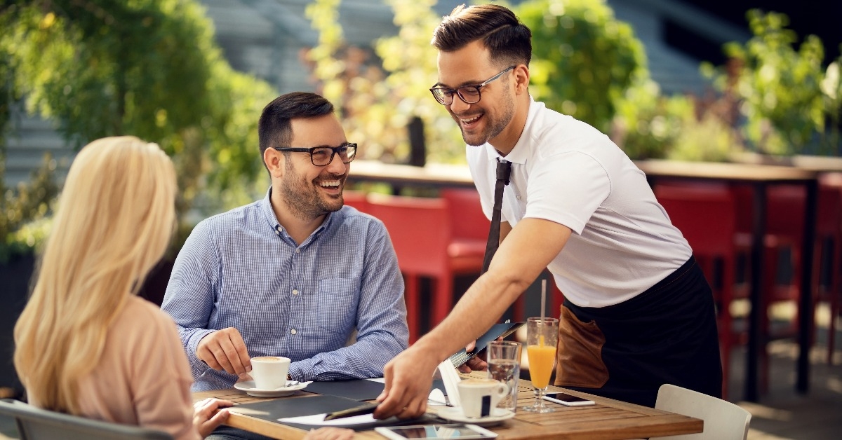 happy waiter setting the table for lunch to a couple in a restaurant
