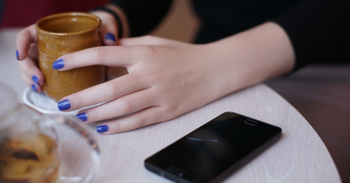 Phone on top of the restaurant table along with hands and beverage 