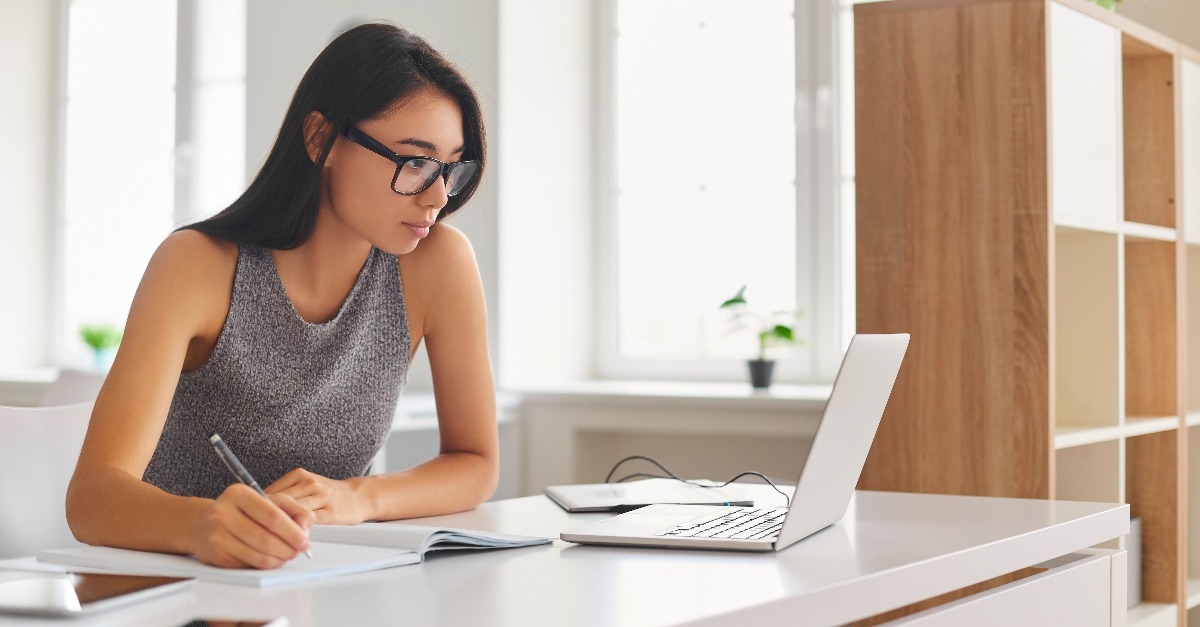 student taking notes in notebook and using laptop 