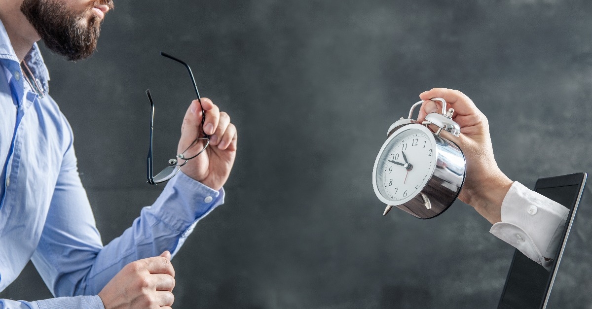 businessman is looking at the hand with clock coming out of the laptop