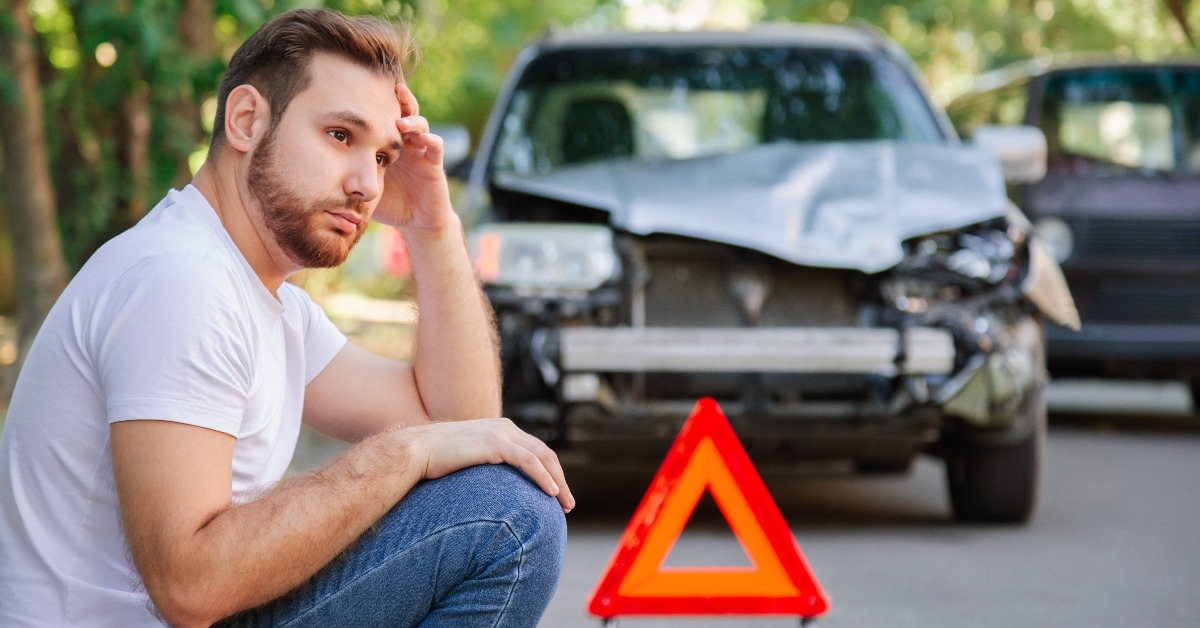 upset man sitting on road near wrecked car after car accident 