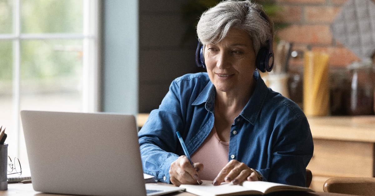 woman sitting at the table wearing headphones while taking notes
