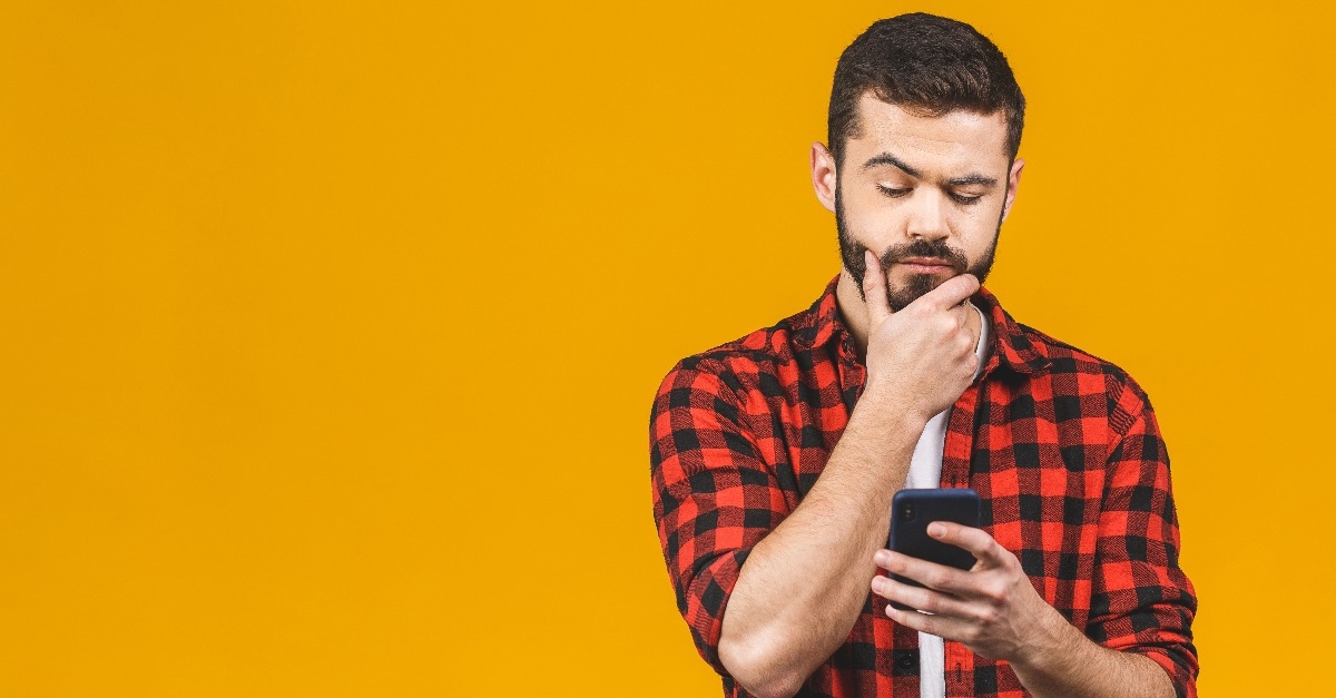 young man thinking while holding smartphone