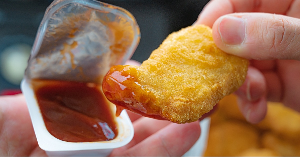 hand holding a chicken nugget dipped in red sauce