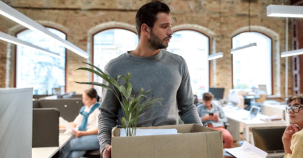 upset man in casual wear holding box with things and leaving the office