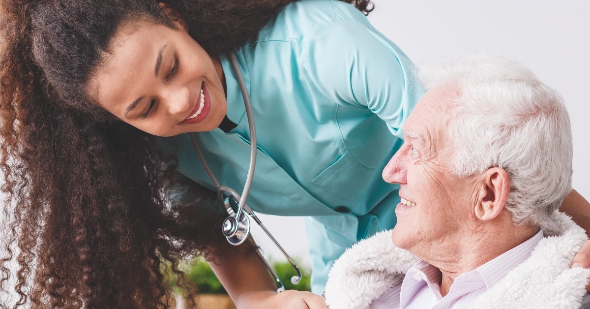  happy nurse with a stethoscope covering an elderly man with a blanket 
