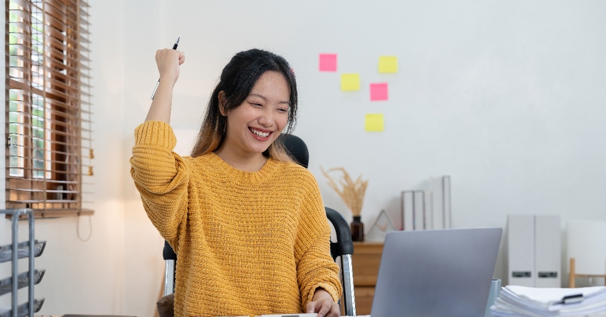 cheerful young female sitting at desk with calculator and laptop