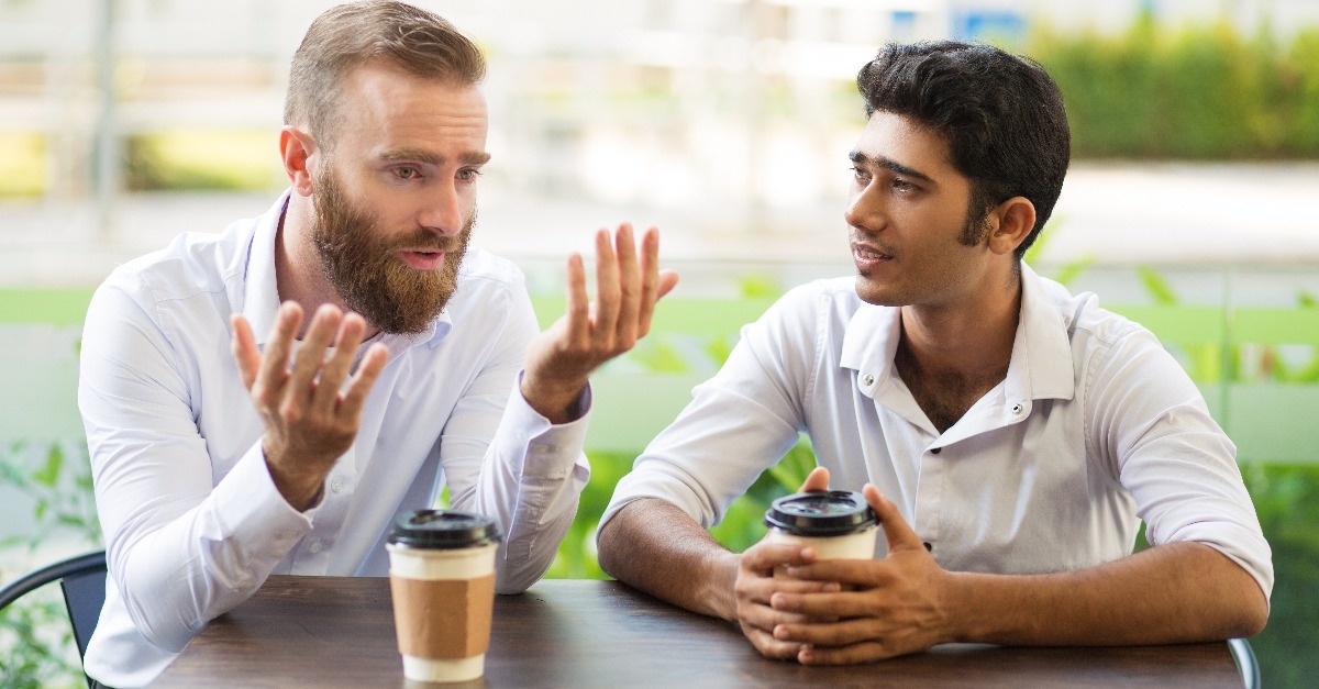 two male friends drinking coffee and talking in an outdoor cafe