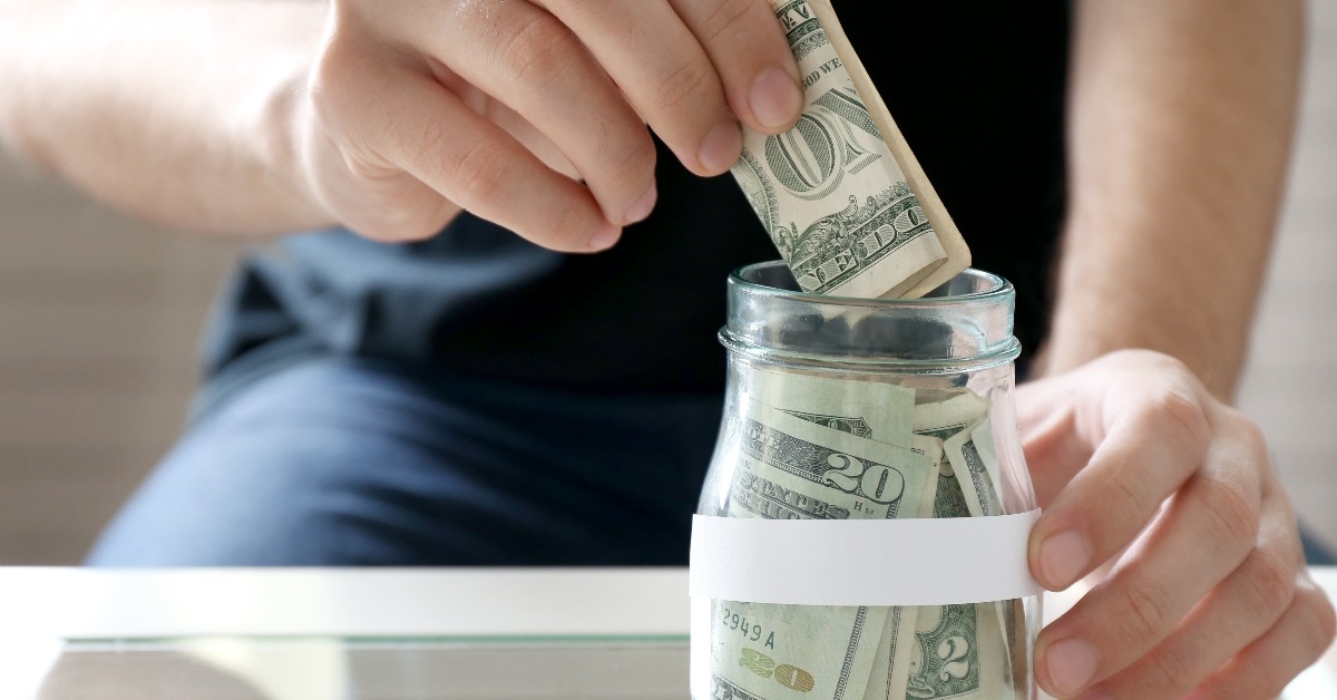 man hand putting money in glass jar