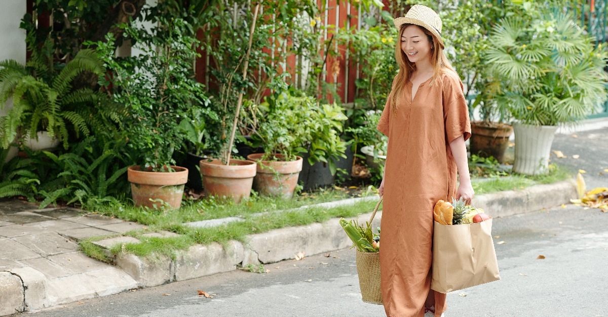 woman in hat and linen dress walking home after shopping