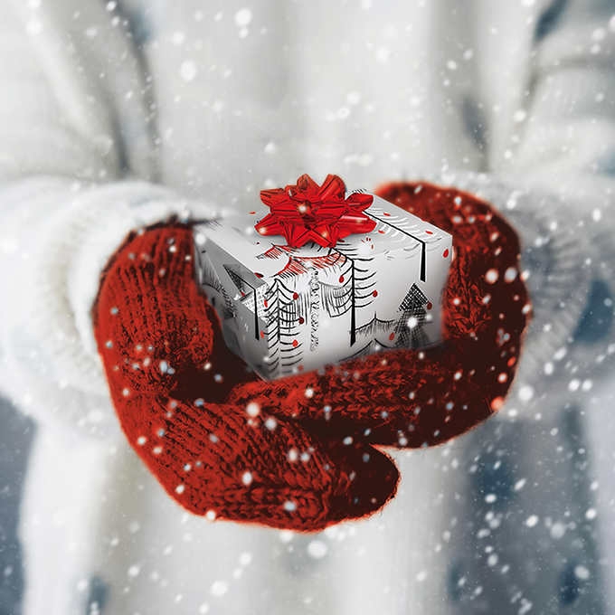 Hands wearing red gloves holding a Christmas gift box in the snow