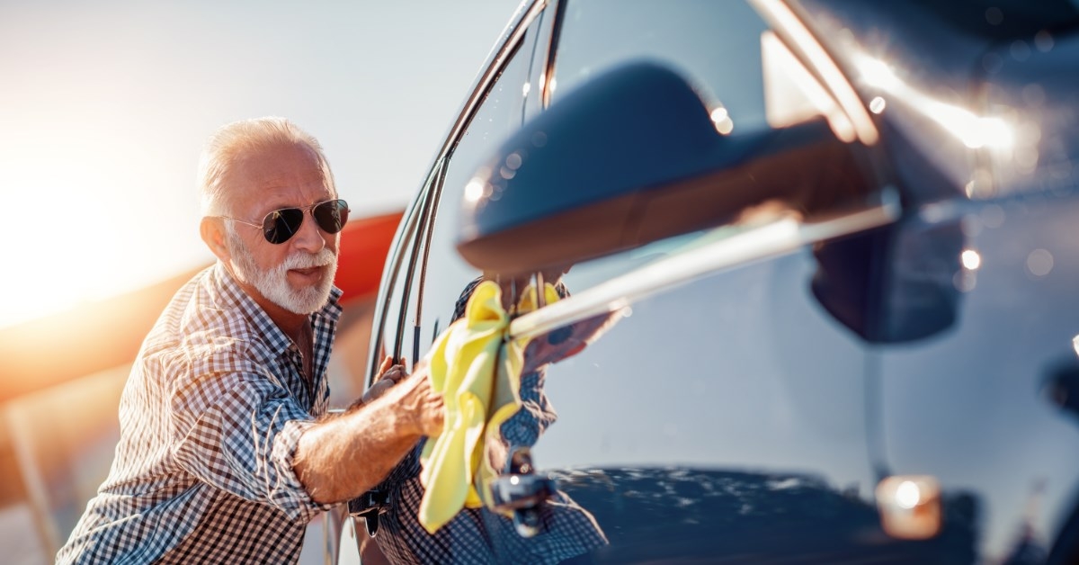old man wearing sunglasses cleaning his car out in the sun