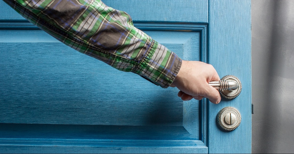 man holding on to by its metal handle in the open wooden door blue