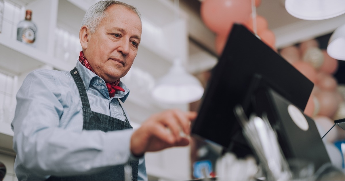 senior man in denim apron working with digital cash register