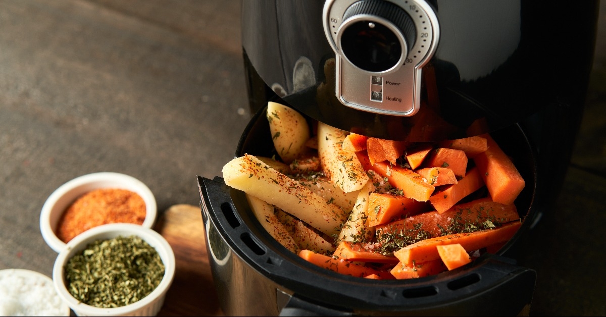 cooking potatoes and carrot sticks with spices in an air fryer