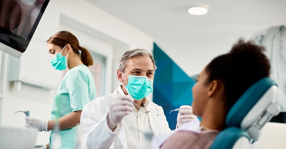 dentist with face mask talking to a female patient during dental procedure 