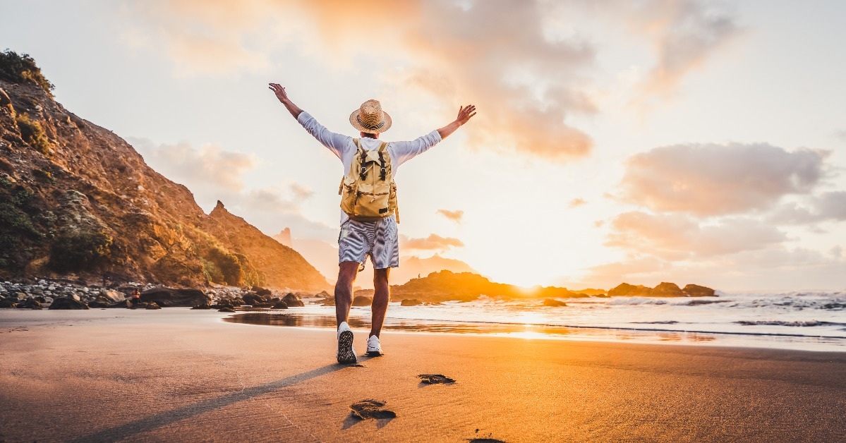 man arms outstretched by the sea at sunrise