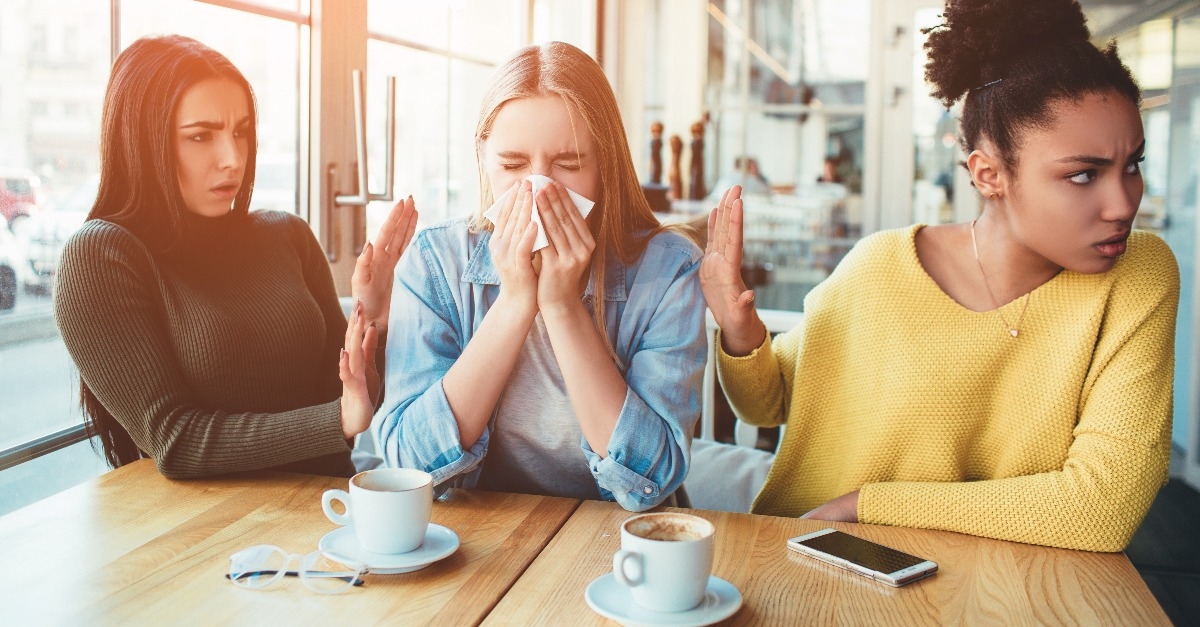 one girl is sneezing between two of her friends