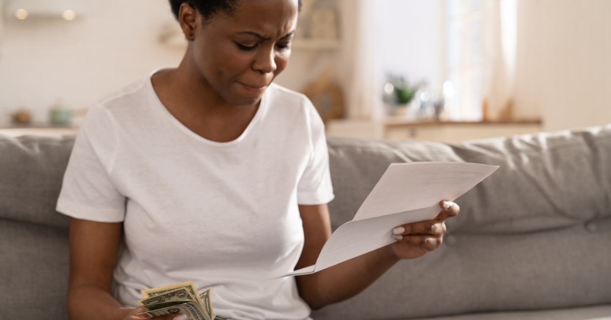 worried african american woman looking at documents while holding money