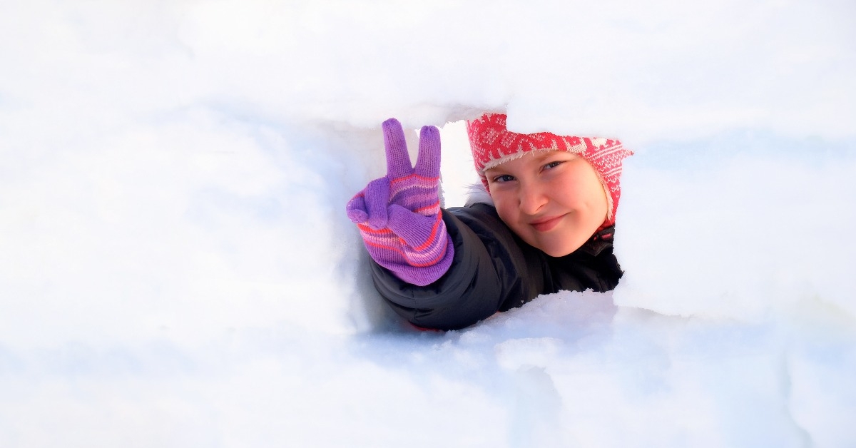 girl in warm winter clothes with a smile looks out of the window of a snowy house
