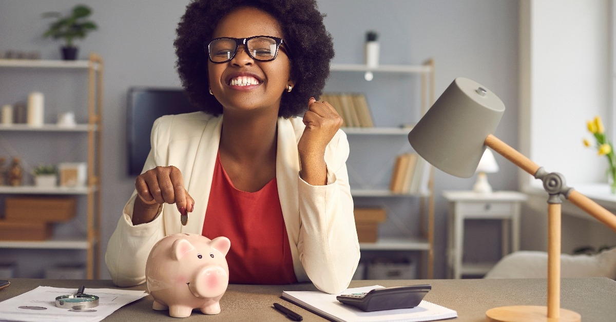 woman in eyewear with yes gesture putting coin into piggybank