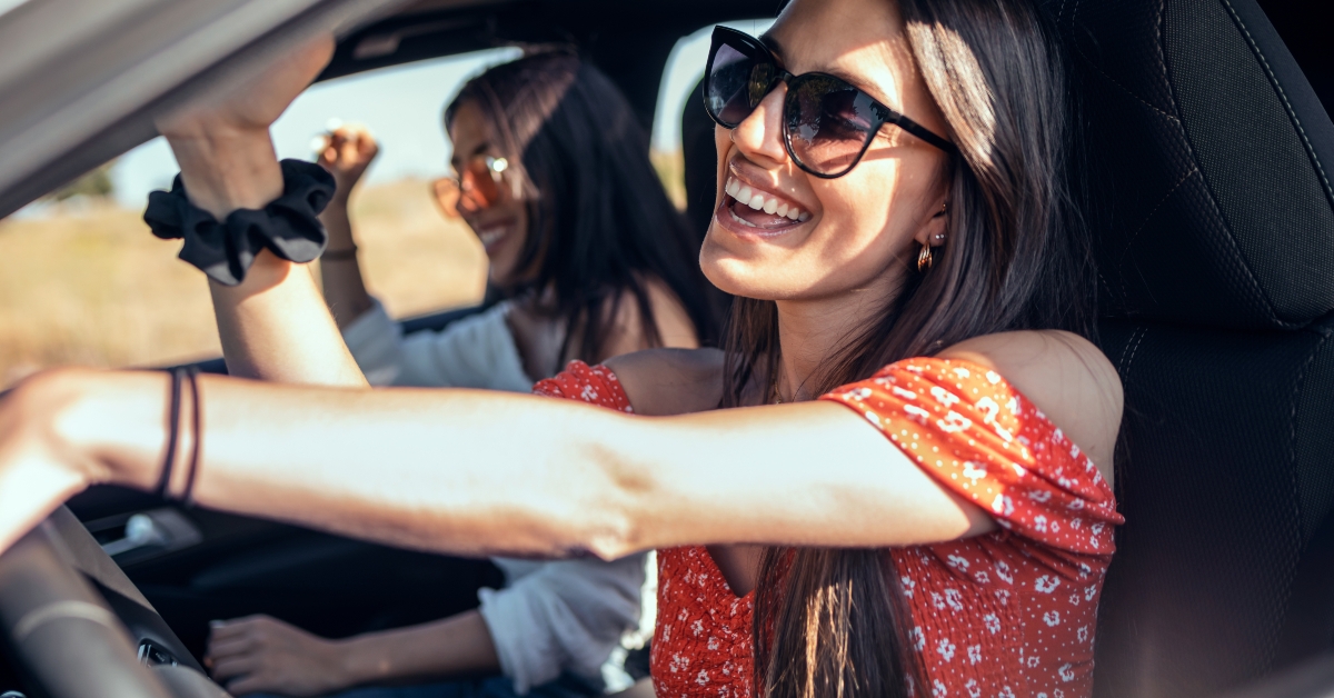 young women singing while driving a car on road trip 
