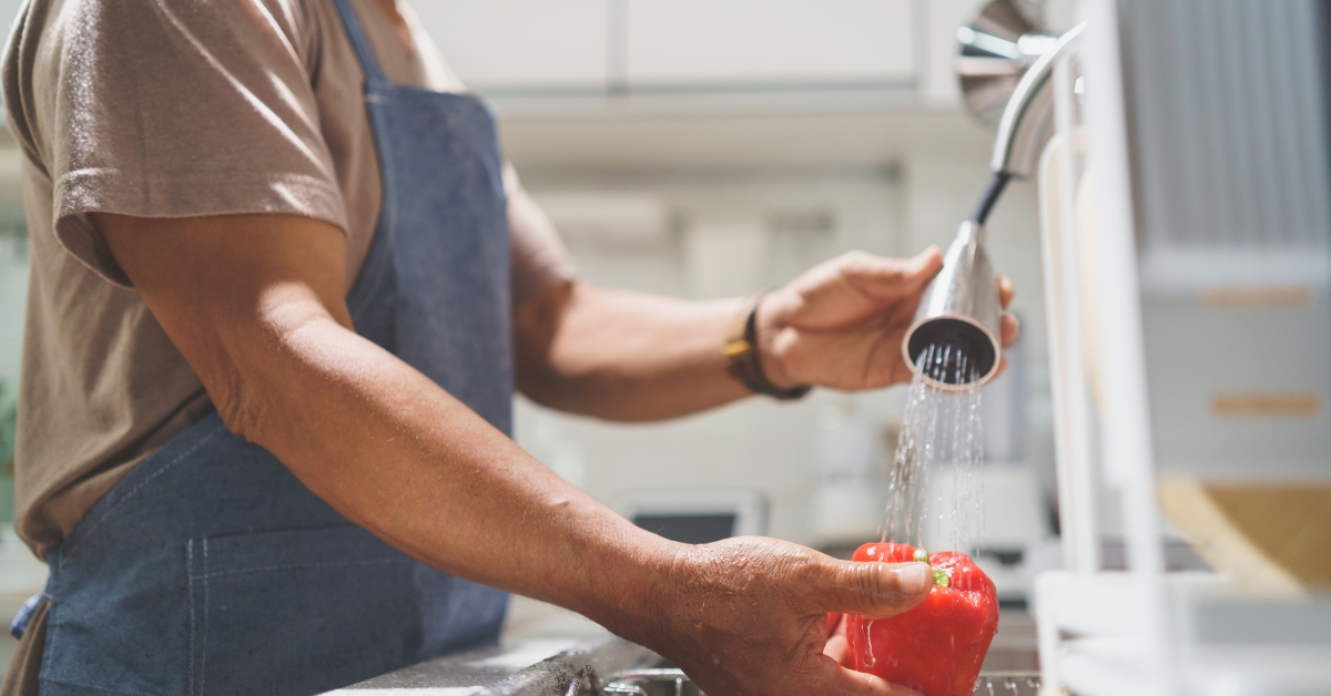 senior man washing fresh red bell pepper