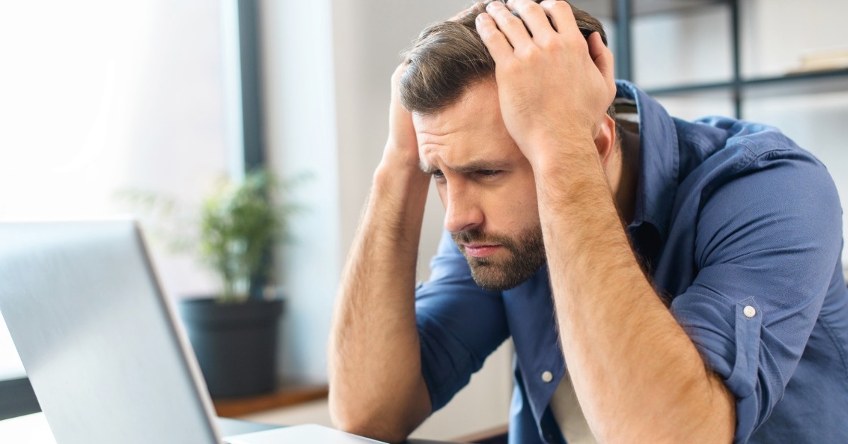 man holding head while frowning at the laptop