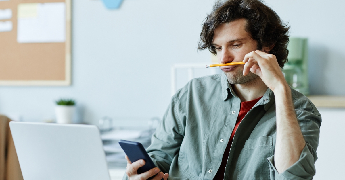 young man playing with pencil and using phone at workplace