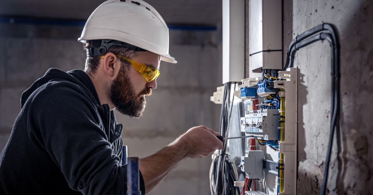 male electrician works in a switchboard with an electrical connecting cable
