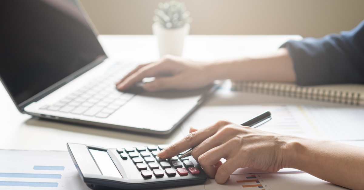 man typing on laptop while using calculator