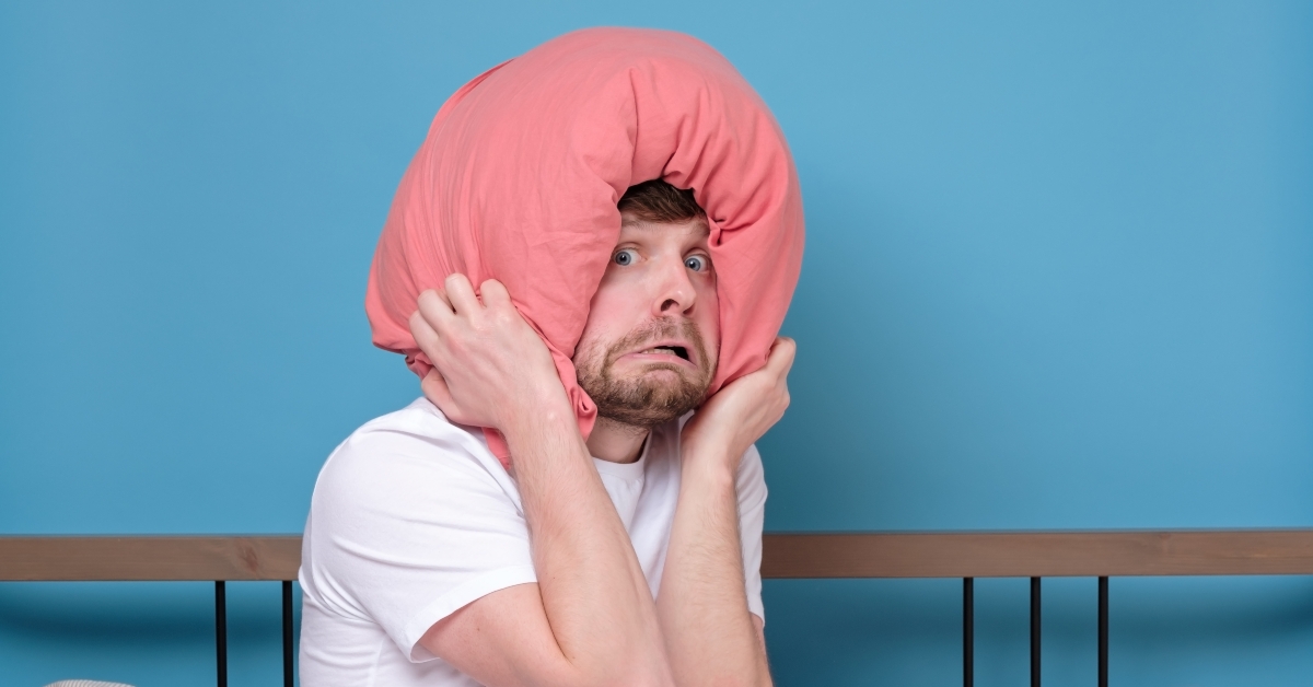 man with pillow on head in bed being afraid