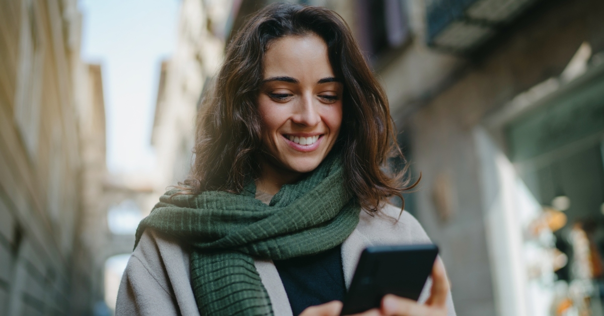 smiling dark-haired woman wearing light-colored coat and green scarf