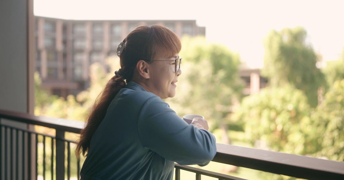 asian senior woman holding a cup of tea looking down from balcony