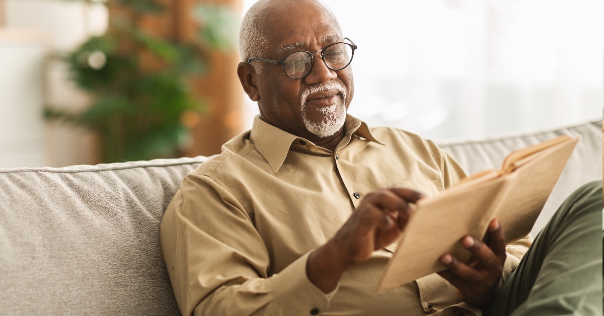 elderly african american man reading book while sitting on couch at home