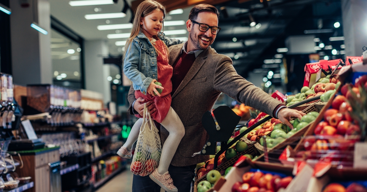 father and daughter buying apples in grocery store