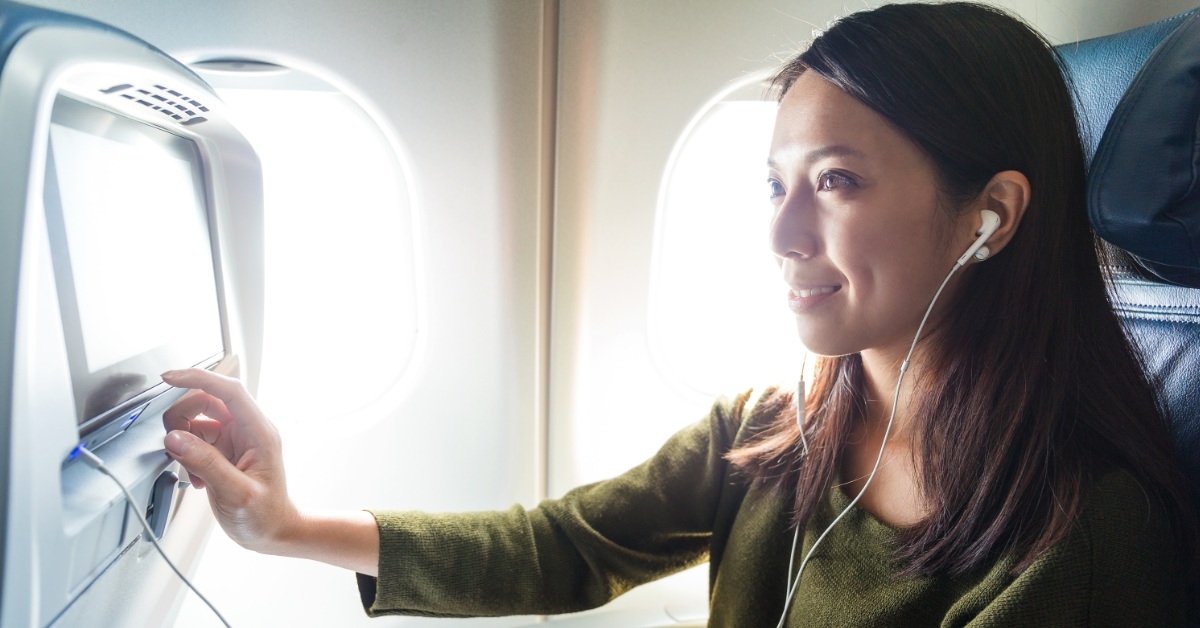 woman wearing headphones happily watching tv on plane 
